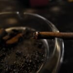 Detailed shot of a cigarette burning in a glass ashtray, symbolizing smoking habit.