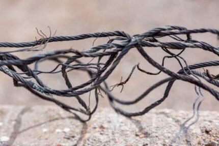 Detailed view of frayed and intertwined steel cables on a blurred background.