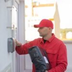 Courier in red uniform delivering a package to a house in Portugal during the day.