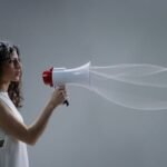 Woman using a megaphone emitting sound waves on a gray background.